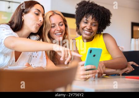 three happy teenage friends using smartphone app in a restaurant Stock Photo