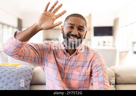 Sitting on couch, waving hand and smiling, indian man relaxing at home, on video call Stock Photo
