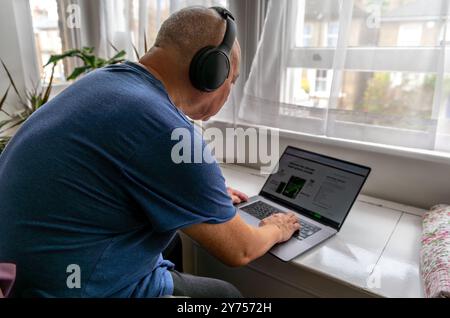 A senior man at home with a wireless headphone and a laptop computer, learning and try to keep up to date with modern technology. A technology use con Stock Photo