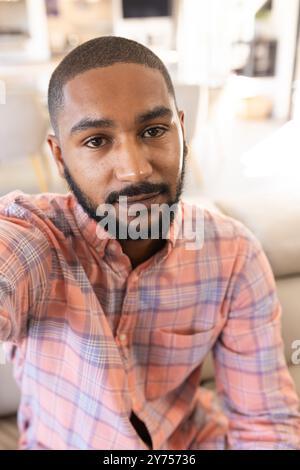 Taking selfie, smiling indian man in plaid shirt at home, on video call Stock Photo