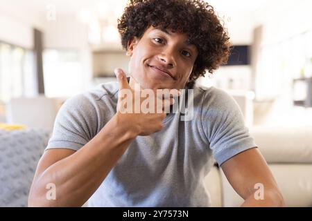 On video call, Smiling man sitting on couch, posing playfully with hand on chin, at home Stock Photo