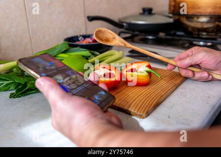 A technology use concept with a person preparing a meal in the kitchen by following an online recipe on a smartphone. Stock Photo