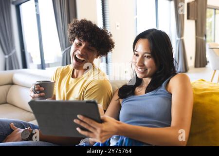 Diverse friends hanging out, laughing and watching something on tablet in living room, at home Stock Photo