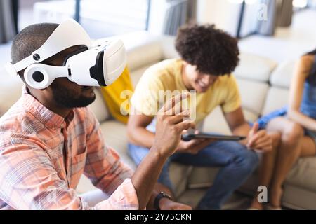 Using VR headset, man interacting with virtual environment while friend using tablet, at home Stock Photo