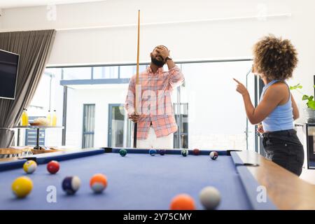 Playing pool, man covering face while woman pointing and laughing, at home Stock Photo