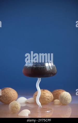 Elegant burgundy cocktail set in a glass with a graceful white wavy stem, placed against a deep blue background, embodying refined luxury Stock Photo