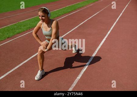 A Young Woman Actively Engaging in Stretching Exercises on a Running Track While Wearing Headphones Stock Photo