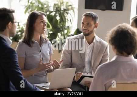 Engaged Caucasian businesswoman with laptop sharing ideas with colleagues Stock Photo