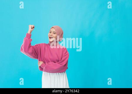 A Confident Young Woman Celebrating Her Success while Dressed in a Bright Pink Sweater and Hijab Stock Photo