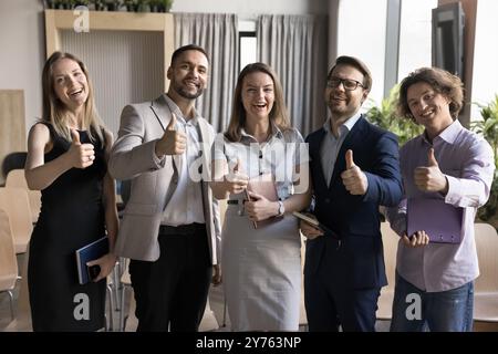 Happy business team making thumb up gesture, looking at camera Stock Photo