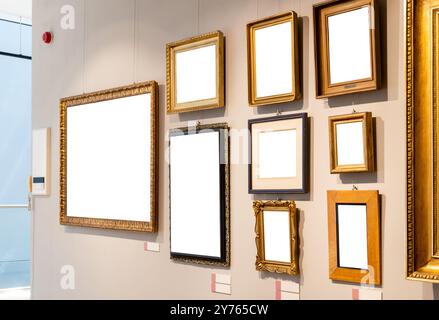 Lots of empty blank cut out white gold painting frames hanging on a wall inside a modern museum or art gallery generic interior, many paintings on one Stock Photo