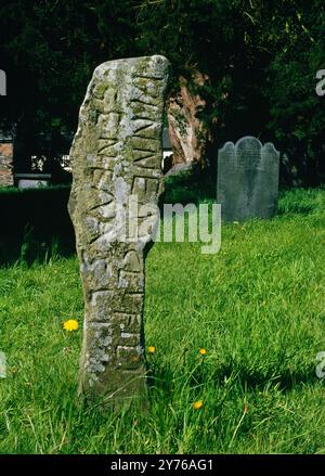 Inscribed stone at the W end of a row of four small standing stones running E-W beside the N wall of St Winifred's Church, Gwytherin, Conwy, Wales, UK Stock Photo