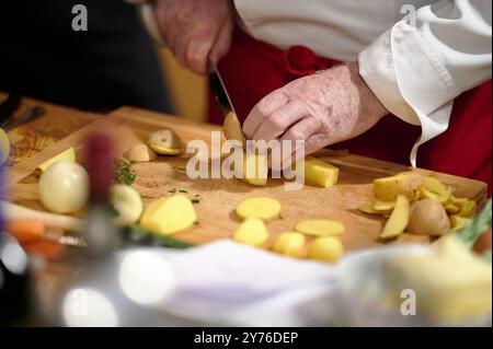 1. Cutting yellow potatoes on a wooden board by a chef in white and red uniform during a cooking class or preparation event Stock Photo