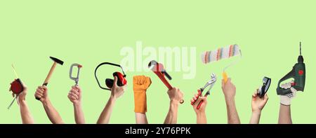 Hands of people with different tools on light green background Stock Photo