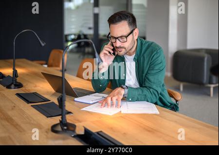 Focused male manager discussing over smart phone while examining revenue reports at desk in office Stock Photo