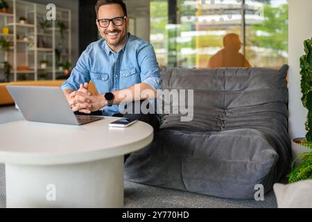 Portrait of confident handsome professional working over laptop while sitting on sofa in modern office Stock Photo