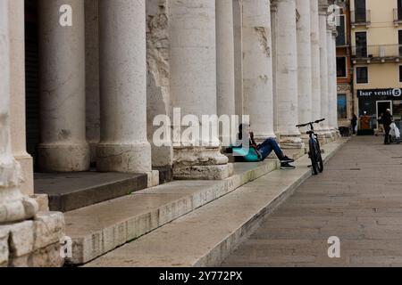 Vicenza, Italy - September 13, 2024: A Deliveroo worker takes a break sitting on the stairs, leaning against his work bag with his bicycle resting aga Stock Photo