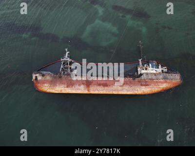 Top view of an old tanker that ran aground, overturned and polluted the coast with oil spilled from it. Ecological catastrophe Stock Photo