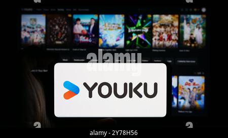 In this photo illustration, a person is holding a cellphone with the logo of Chinese video hosting company Youku Tudou Inc. in front of business webpage. Stock Photo