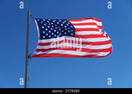 tattered United States of America flag flapping in the wind with blue sky background Stock Photo