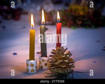 Three burning advent candles in decorative holders with pine cones and festive bokeh background. Stock Photo