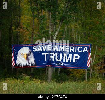 Tyngsborough (Tyngsboro), MA, USA. Large Pro-Trump 2024 sign hung on the right side of the North bound lanes of Interstate 95 (I-95), before the 5 November 2024 U.S. Presidential election.  The sign on vacant forested land is along I-95 near the Massachusetts New Hampshire border close to Tyngsboro, MA.  The large sign, about the size of a shipping container, 40 ft (12.2 meters) by 8.5 ft (2.60 meters), is suspended by cable over trees about 200 feet (60 meters) from the Interstate. Stock Photo