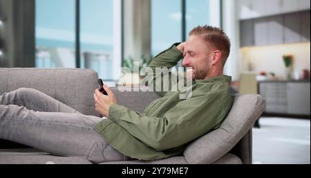 Young Happy Man Using Mobile Phone Lying On Sofa Stock Photo