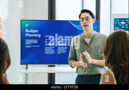 asian leader presenting a financial data and strategies in a modern office with charts and graphs displayed on a large screen Stock Photo