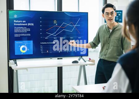 asian leader presenting a financial data and strategies in a modern office with charts and graphs displayed on a large screen Stock Photo