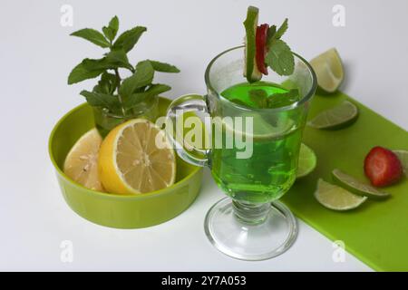 Green lemonade in a glass. Decorated with lime and strawberries. With sprigs of mint. Near lemon and mint. Stock Photo