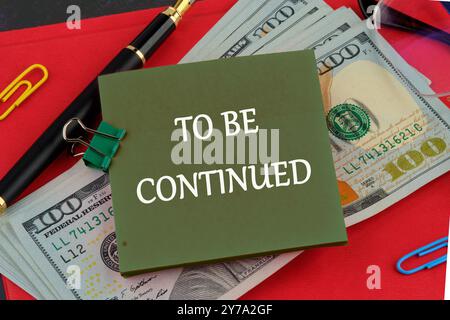 TO BE CONTINUED text written on a green sticker on the background of dollar bills on the red book Stock Photo