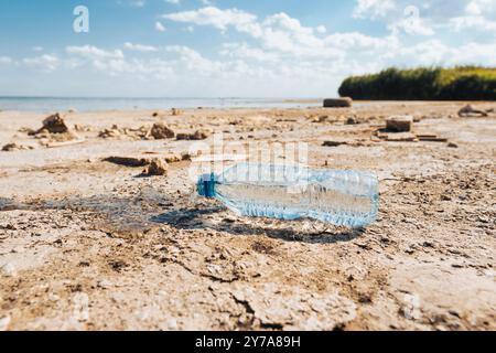Plastic bottle with water leaking out lies on the bottom of a dry lake on a sunny summer day. Conceptualization of climate change and drought Stock Photo