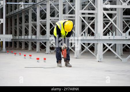 Worker drilling holes for chemical anchors in concrete foundation slab on construction site of rack-supported structure Stock Photo