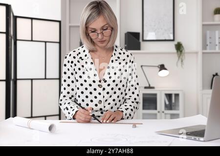 Architect making engineering drawing at table in office Stock Photo