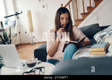 Thoughtful young woman writing something down while resting at home Stock Photo