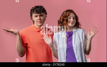 Confused stylish couple shoulders up - can't help, makes gesture of dont know. Difficult question, guilty reaction, puzzled man and woman on pink back Stock Photo