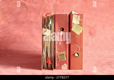 Row of messy file folders,grungy old business papers,red tape, bureaucracy,chaotic business management,concept.Red background, free copy space. Stock Photo