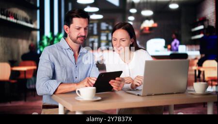 Coworkers Using Technology Lifestyle. Man And Woman Drinking Coffee In Cafe Stock Photo
