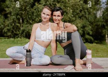 Portrait of beautiful mother and her beloved daughter sitting on yoga mat after train and posing for photo together Stock Photo