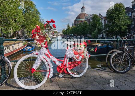 Colourful bike decorated with flowers on a bridge over the Singel canal, Old Round Lutheran church in the background, in Amsterdam, the Netherlands Stock Photo