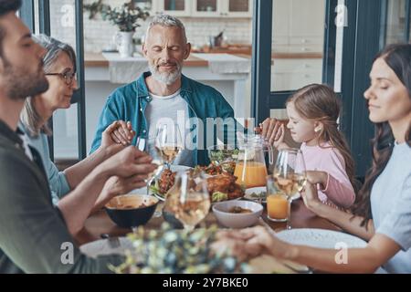 Happy multi-generation family holding hands and praying before having dinner Stock Photo