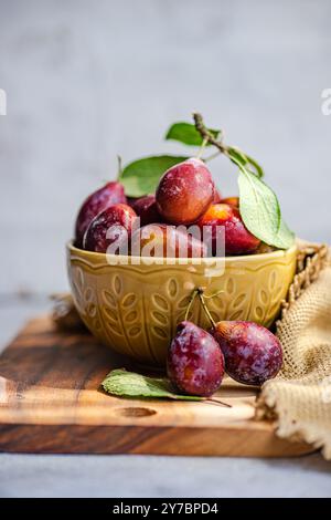 Close-up of a bowl fresh red plums on wooden chopping board Stock Photo