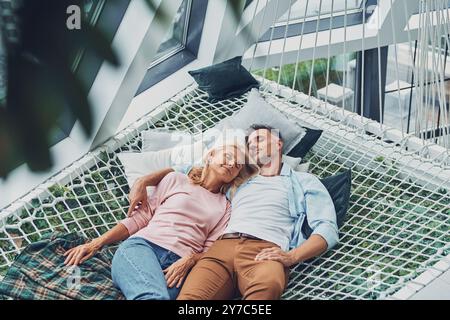 Top view of beautiful mature couple sleeping while lying down in big hammock at home together Stock Photo