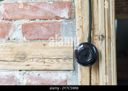 Vintage electrical switch, light button with black electric cable mounted on a half-timbered or timber-framed wall. Stock Photo