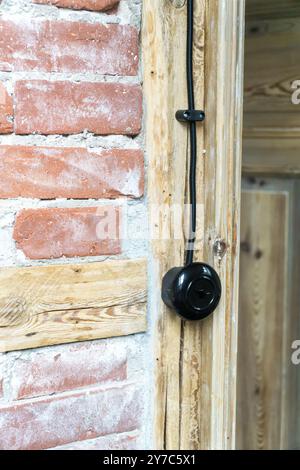Vintage electrical switch, light button with black electric cable mounted on a half-timbered or timber-framed wall. Stock Photo
