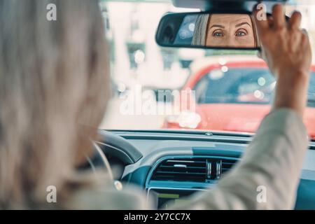 Rear view of mature beautiful woman in smart casual wear adjusting back view mirror while driving car Stock Photo