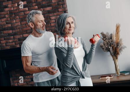 Modern senior couple in sports clothing exercising and using hand weight while spending time at home Stock Photo
