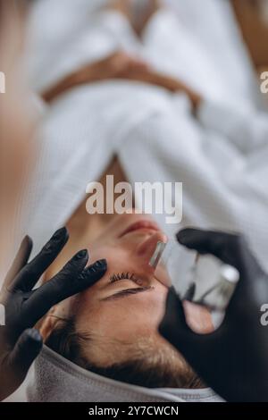 Cosmetologist making facial treatment with ultrasonic spatula to young woman. Stock Photo