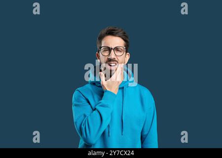 A man wearing a blue hoodie displays a pained expression while holding his chin Stock Photo