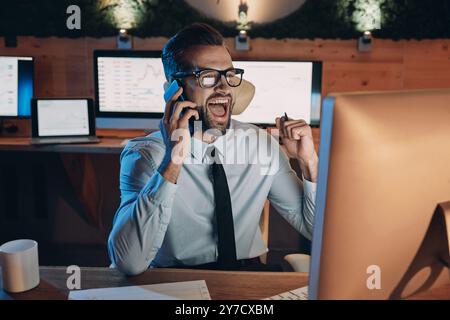 Happy young man talking on mobile phone and gesturing while staying late in the office Stock Photo